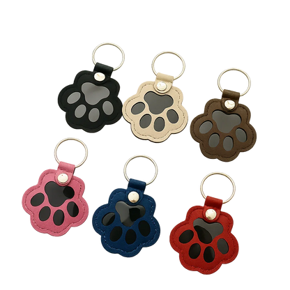 Custom paw-shaped leather pet fur keepsake keychain in black, beige, and brown, featuring a transparent window for fur storage and a personalized portrait on the back.