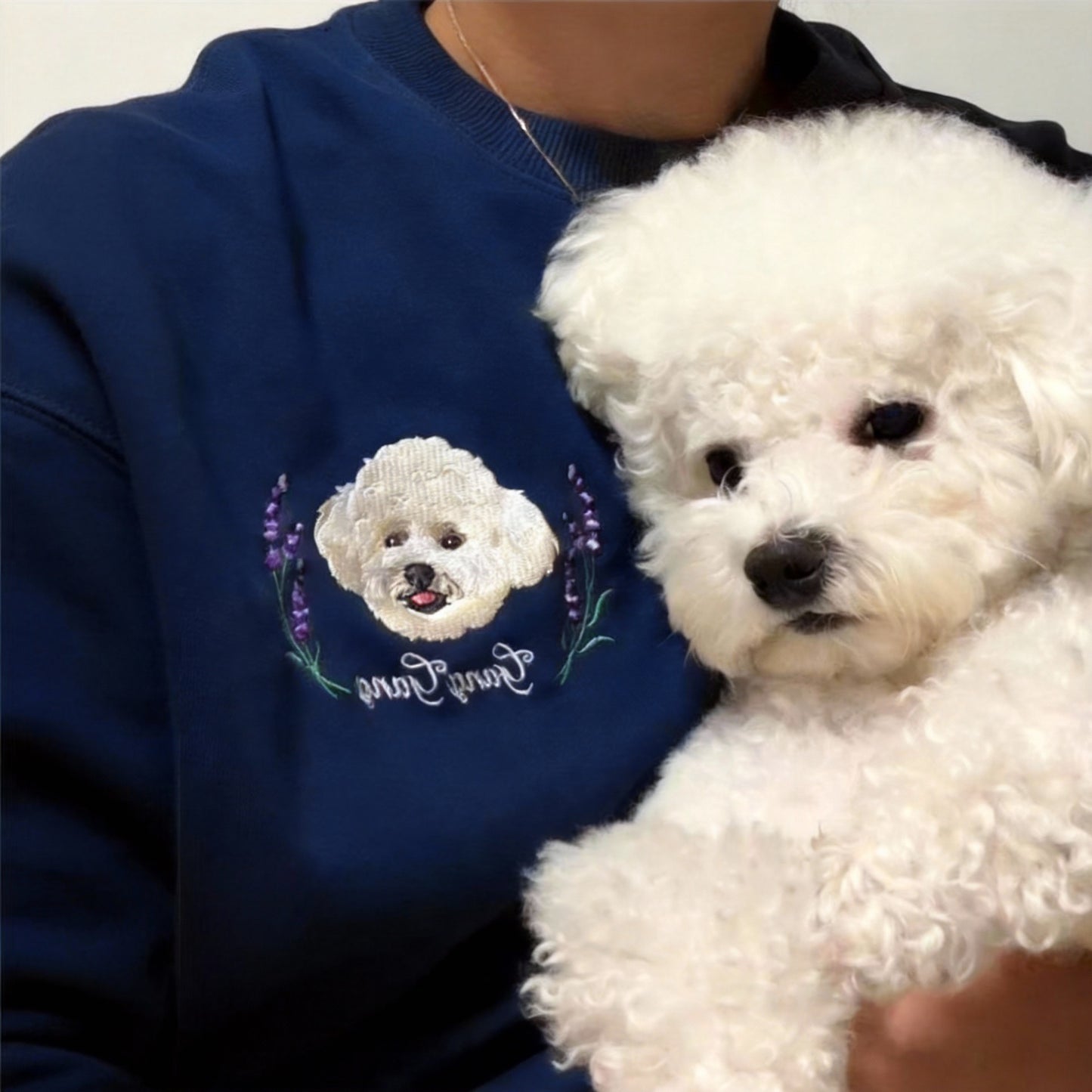 Model wearing a navy blue custom pet portrait sweatshirt while holding a white Bichon Frise dog