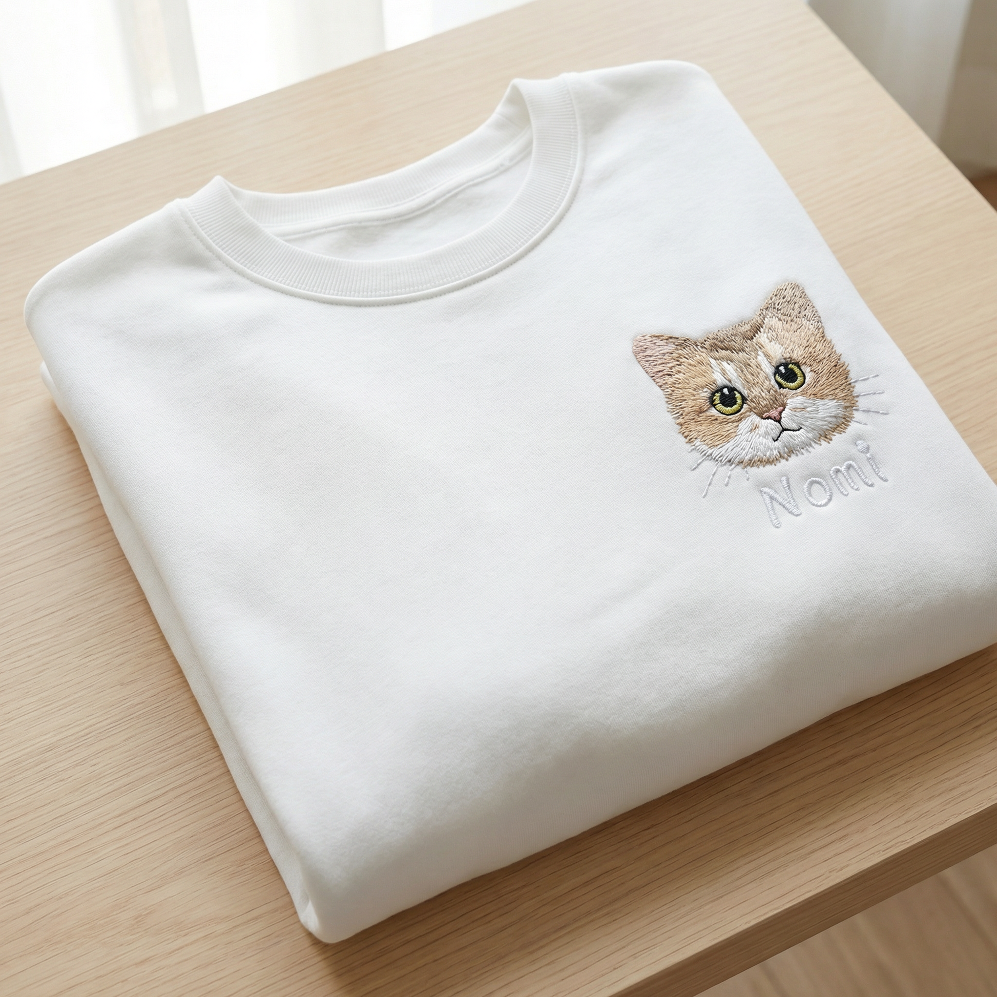 Folded white custom embroidered pet sweatshirt showing a detailed cat portrait and name - premium pet lover gift