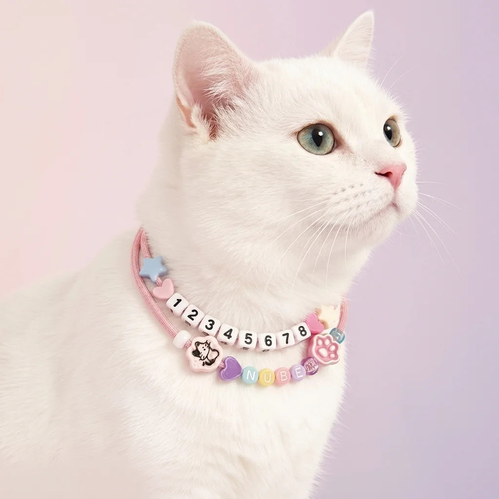 Elegant white cat wearing a personalized pink-themed bead necklace with its name, demonstrating pet jewelry for cats.